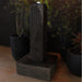 Side view of Yang sculptural outdoor water fountain with curved stone design and square base, styled among potted plants at night.