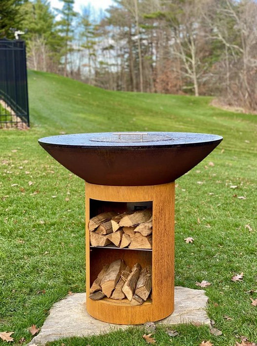 Backyard setting of an Arteflame Classic 40" Grill and Tall Base with logs in the Storage.