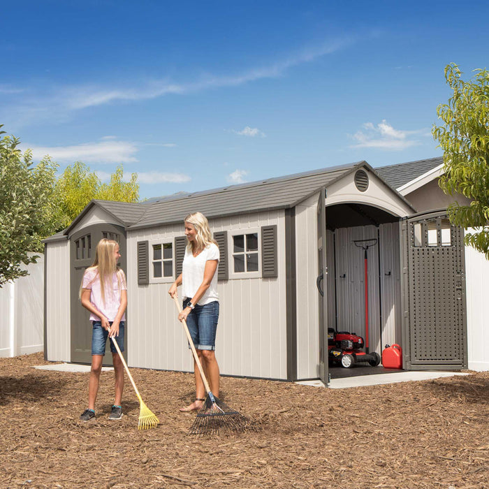 Two women interacting beside a storage shed with doors open.