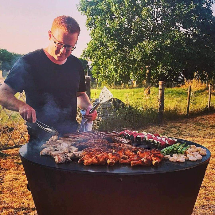 A person grilling a feast on an Arteflame One Series 40" grill at sunset in a rural backyard.