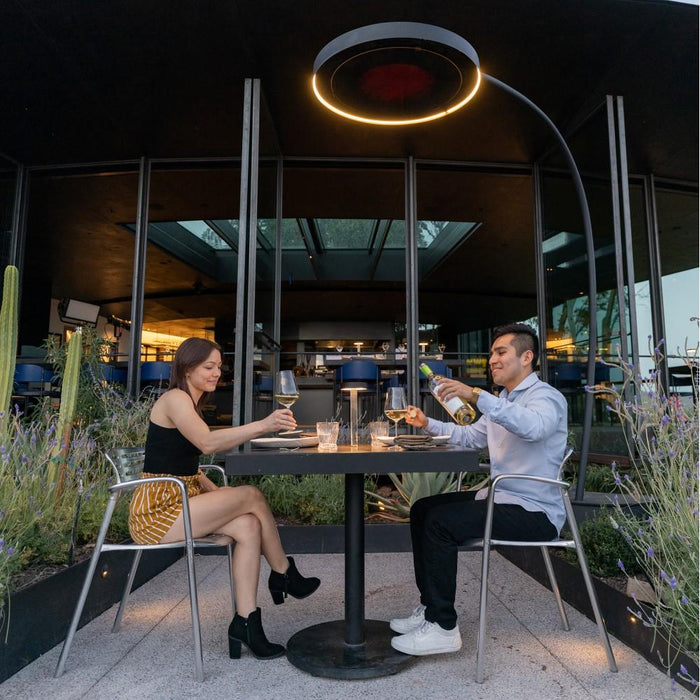 A couple enjoying an intimate outdoor dinner under the warmth of a Bromic Eclipse Smart-Heat 2900W Electric Portable Freestanding Heater with Dimmer Control.