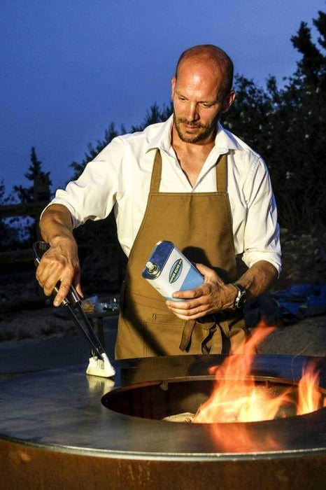 A chef seasoning the cooktop of an Arteflame Classic outdoor grill with a fire bowl feature.