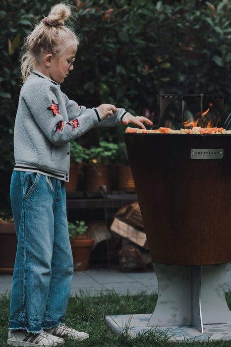 A young child grilling vegetables on the Arteflame 20-inch One Series, showcasing family-friendly outdoor cooking.