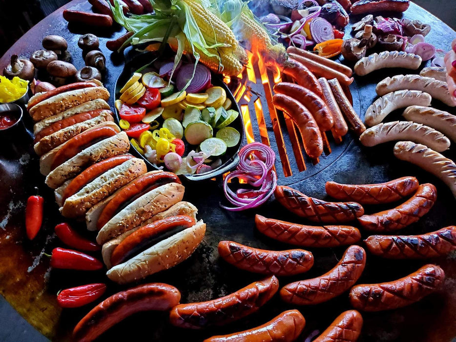 A full meal with sausages, vegetables, and buns grilled on an Arteflame insert in a Kamado grill.
