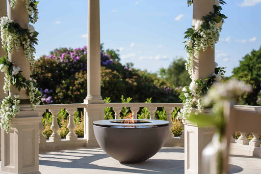The Solus Decor Hemi Firebowl positioned along a garden pathway, serving as a statement piece amidst lush landscaping.