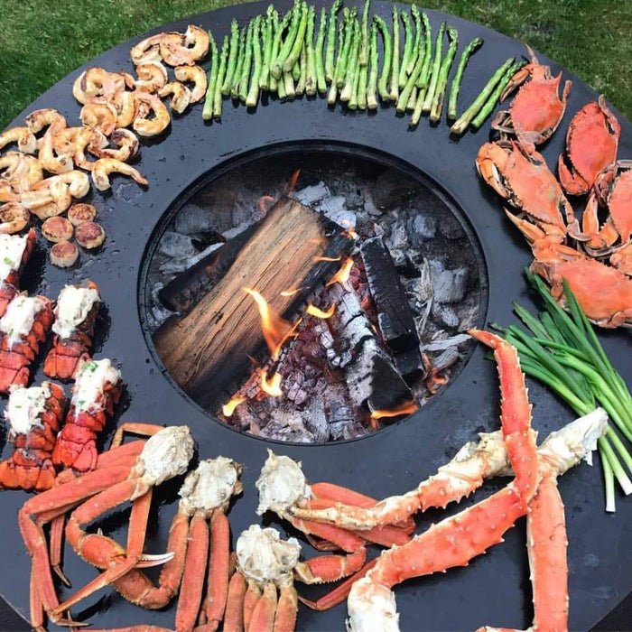 Top view of an Arteflame One Series grill while cooking an array of seafood and vegetables over an open flame.