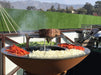 A culinary scene with a steak being grilled alongside vegetables on the Arteflame Classic 40" Grill with a picturesque mountain background.