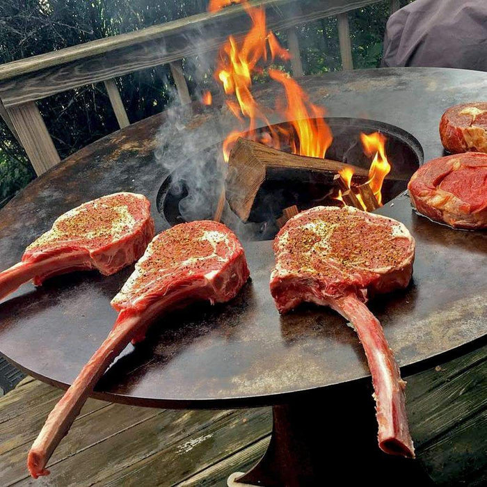 Juicy steaks grilling on the Arteflame Classic's 40" carbon steel cooktop with a sturdy Euro base.