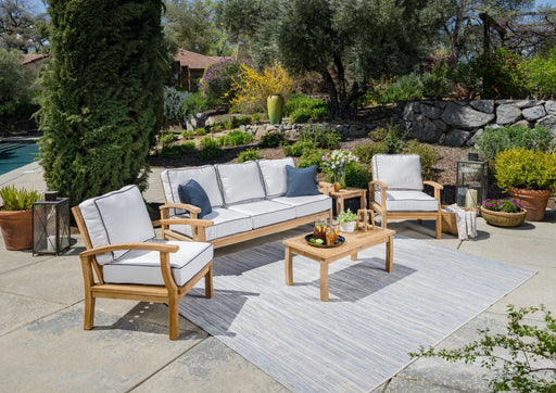 A Tortuga Outdoor 5-Piece Indonesian Teak Sofa Set with Sunbrella Canvas Natural or Navy cushions and a blue rug.