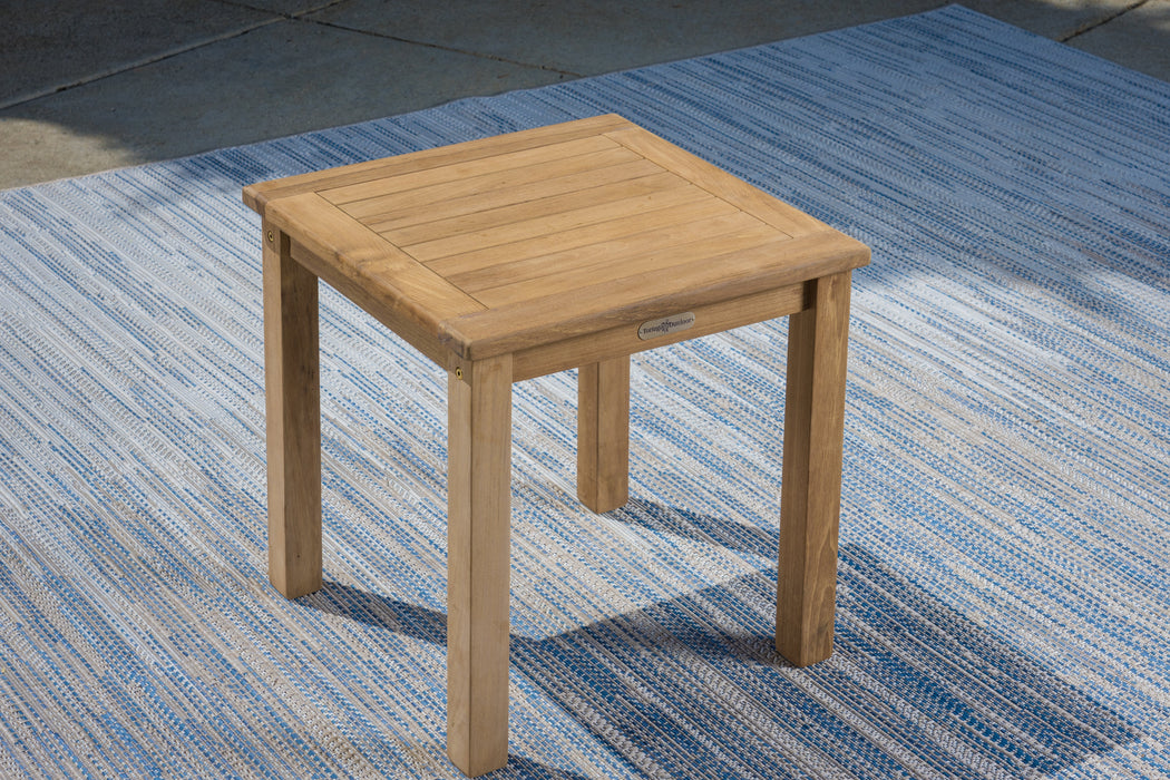 A small Tortuga Outdoor teak side table on a patio.