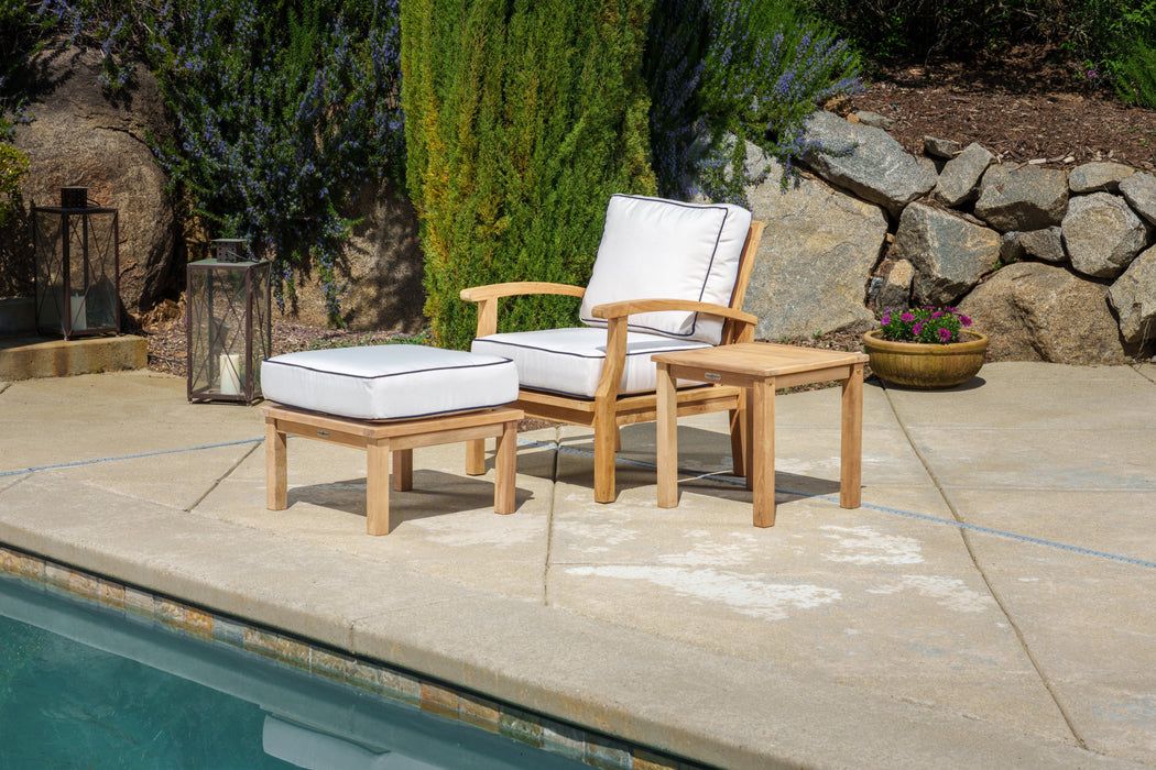 A Tortuga Outdoor 3-Piece Indonesian Teak Club Chair Set - Canvas Natural or Navy with a durable construction and all-weather resin wicker, including a chair and a footstool, is next to a pool.