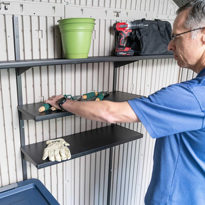 A man is putting tools on a shelf in a Lifetime 8 Ft. X 15 Ft. Outdoor Storage Shed - 60075 by Lifetime.