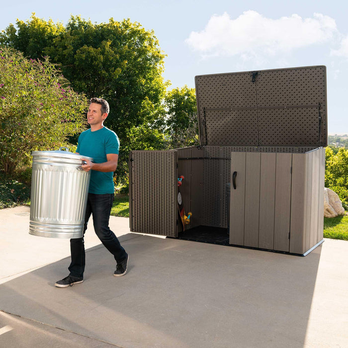 A man carrying a bin out of the Lifetime Horizontal Storage Shed (75 Cubic Feet) - 60341.