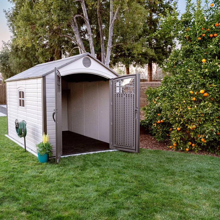 A shed with open doors in a backyard with an orange tree.