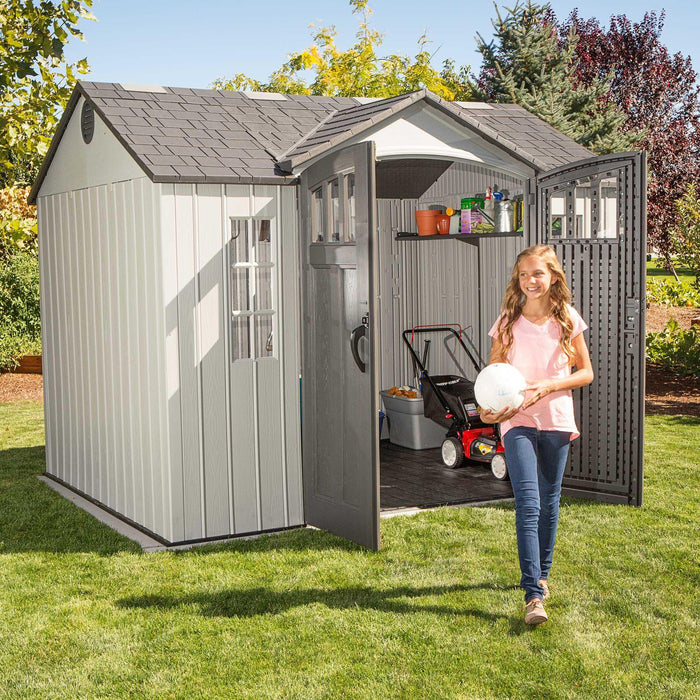 A girl is standing in front of a Lifetime 10 Ft. X 8 Ft. Outdoor Storage Shed - 60243.