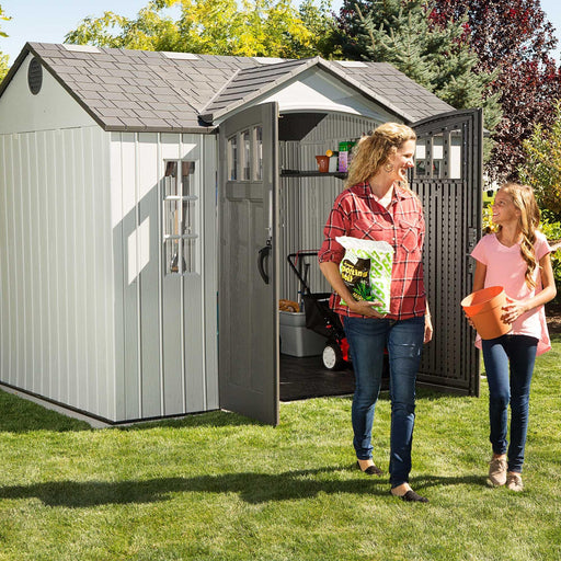 A woman and a girl standing in front of a Lifetime 10 Ft. X 8 Ft. Outdoor Storage Shed - 60243.