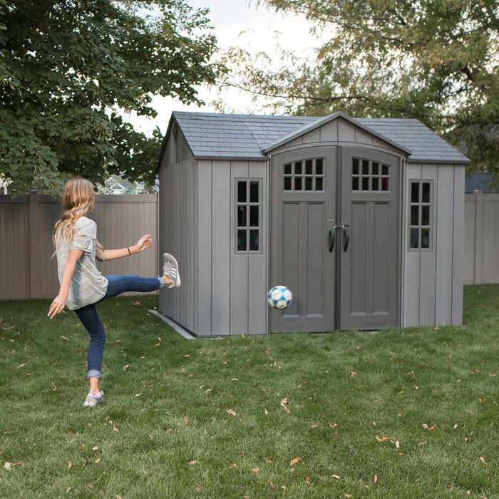 A girl kicking a Lifetime 10 Ft. X 8 Ft. Outdoor Storage Shed - 60330 soccer ball.