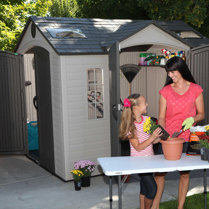 A woman and a girl standing in front of a Lifetime 10 Ft. X 8 Ft. Outdoor Storage Shed - 60001.