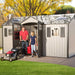A man is pushing a lawnmower in front of a Lifetime 15 Ft. X 8 Ft. Outdoor Storage Shed - 60138.