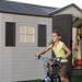 A girl riding a bike in front of a Lifetime 15 Ft. X 8 Ft. Outdoor Storage Shed - 6446.