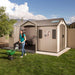 A woman pushing a Lifetime 15 Ft. X 8 Ft. Outdoor Storage Shed - 60079 lawnmower in front of a shed.