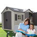 A woman and a girl sitting on a bench reading a Lifetime 15 Ft. X 8 Ft. Outdoor Storage Shed - 60079 book.