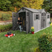 A man is mowing the lawn in front of a Lifetime 15 Ft X 8 Ft Outdoor Storage Shed - 60318.