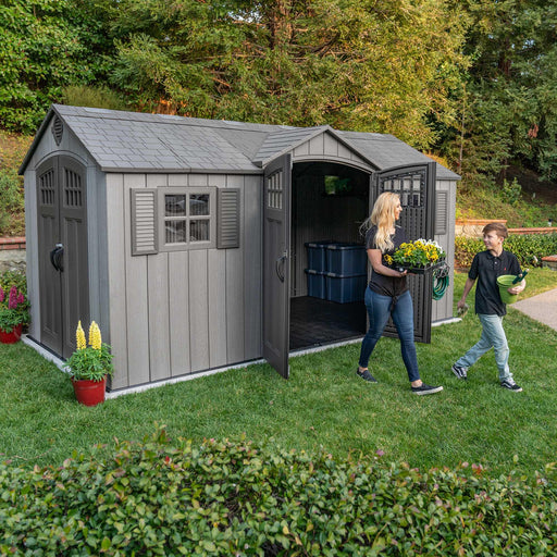 A woman and a child are standing outside of a Lifetime 15 Ft X 8 Ft Outdoor Storage Shed - 60318.