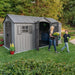 A woman and a child are standing outside of a Lifetime 15 Ft X 8 Ft Outdoor Storage Shed - 60318.