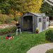 A boy is mowing the lawn in front of a Lifetime 15 Ft X 8 Ft Outdoor Storage Shed - 60318.