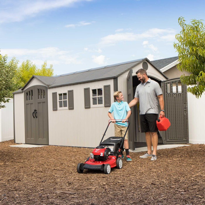 A man and a boy mowing next to a 17.5 Ft. X 8 Ft. Outdoor Storage Shed