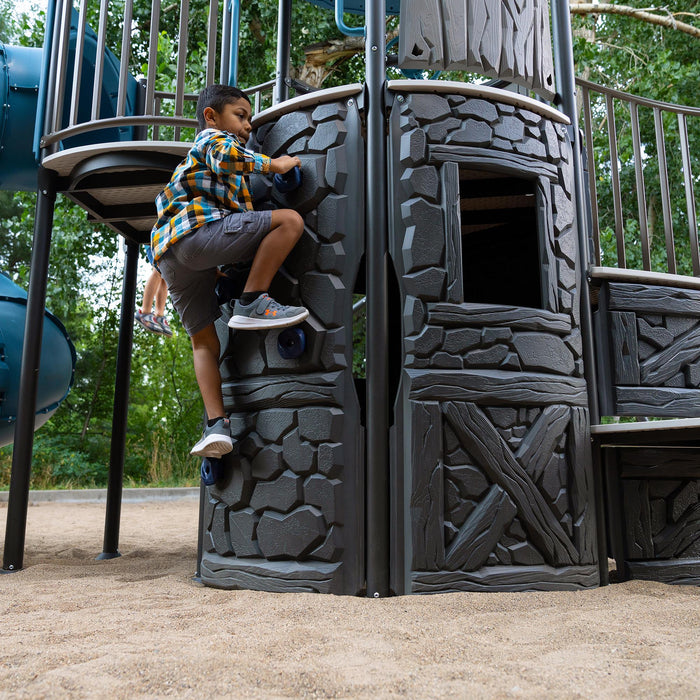 Young child actively climbing the stone-textured wall of the Lifetime Adventure Castle with blue handholds.