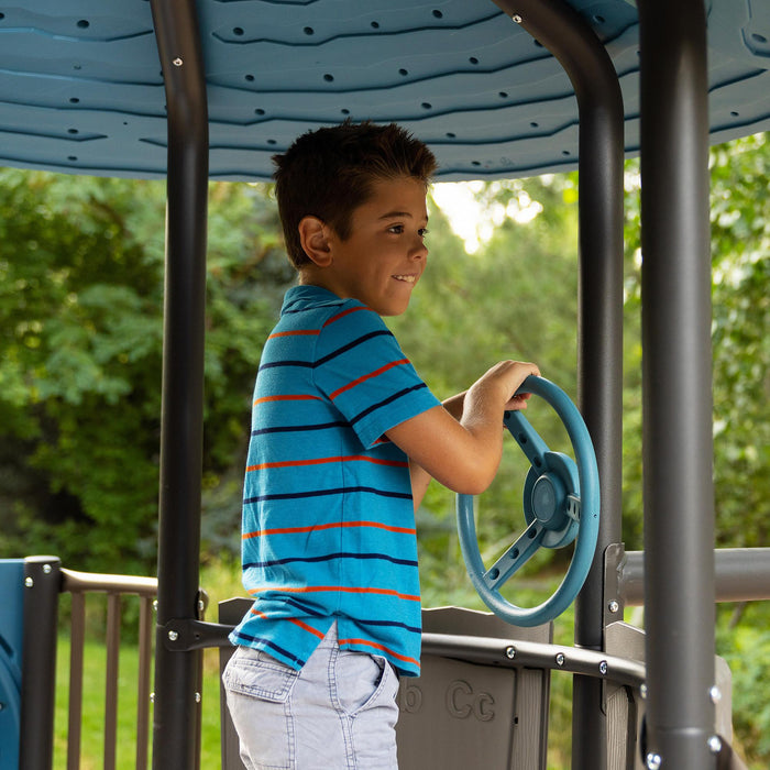 Young boy playing with the steering wheel at the top of the Lifetime Adventure Castle playset.