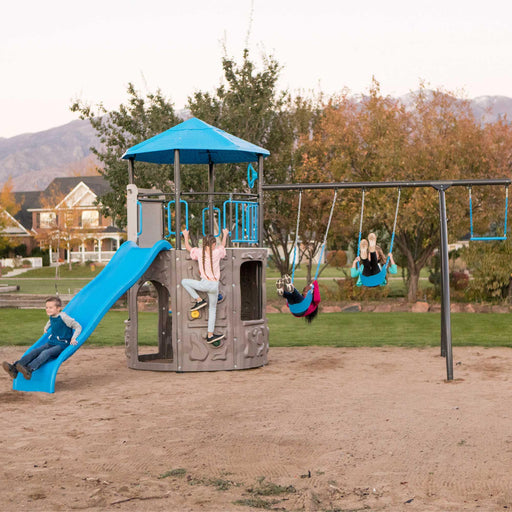 Full view of the Lifetime Adventure Tower playset with children playing on swings and a slide, set against a backdrop of a park and homes.