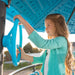 A young girl engaging with a blue steering wheel on the upper platform of the Lifetime Adventure Tower playset during a sunny day.