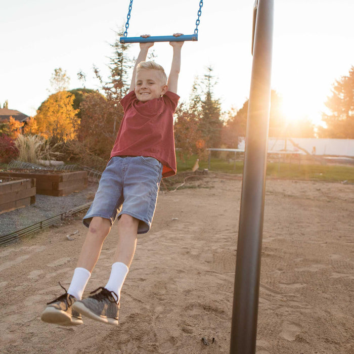 A child in mid-swing on a blue swing of the Lifetime Adventure Tower playset with the sun setting in the background.