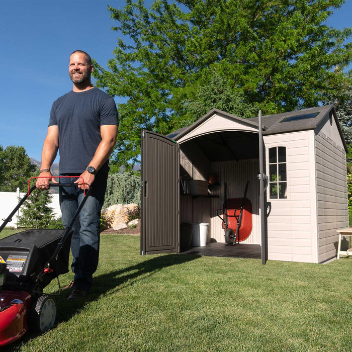 A man with a Lifetime 10 Ft. X 8 Ft. Outdoor Storage Shed - 60005 standing next to a lawn mower.
