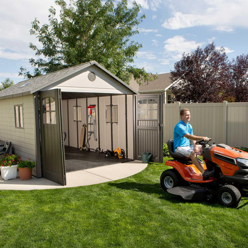A man riding a lawn mower in front of a Lifetime 11 Ft. X 21 Ft. Outdoor Storage Shed - 60237.