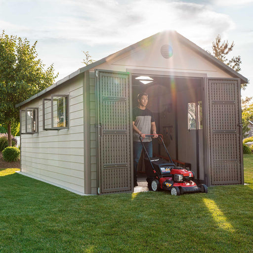 A woman is standing in front of a Lifetime 11 Ft. X 18.5 Ft. Outdoor Storage Shed - 60355 with a lawn mower.