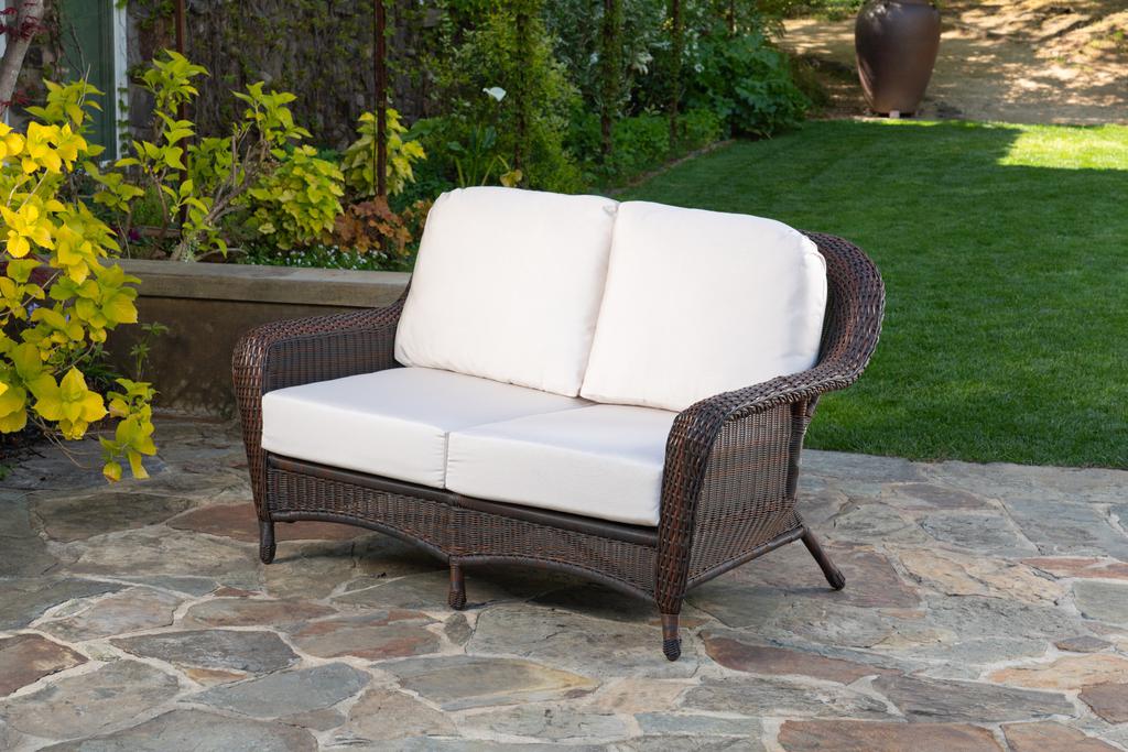 A Tortuga Outdoor Sea Pines Java Loveseat is set on a stone patio, showcasing all-weather resilience.