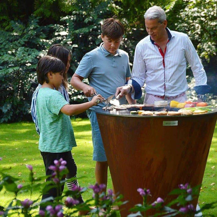 A family cooking together on an Arteflame One Series 40" grill set in a lush garden.