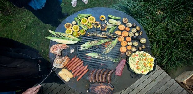 A full spread of meats and vegetables on an Arteflame grill surface, showcasing its large capacity and social grilling potential.