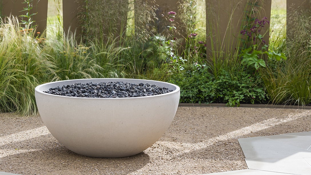 The Solus Decor Hemi Firebowl as a central element in a landscaped garden, enhancing the outdoor appeal with its sleek concrete design.