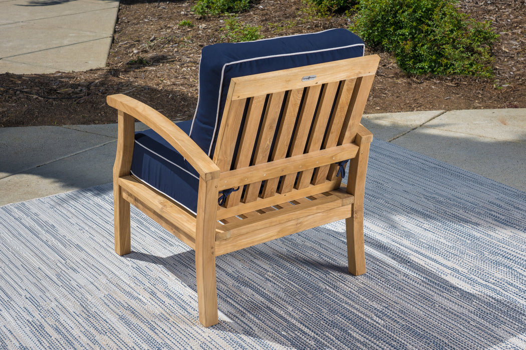 A durable Tortuga Outdoor teak dining chair with an all-weather resin wicker construction, complete with a blue cushion and situated on a rug.