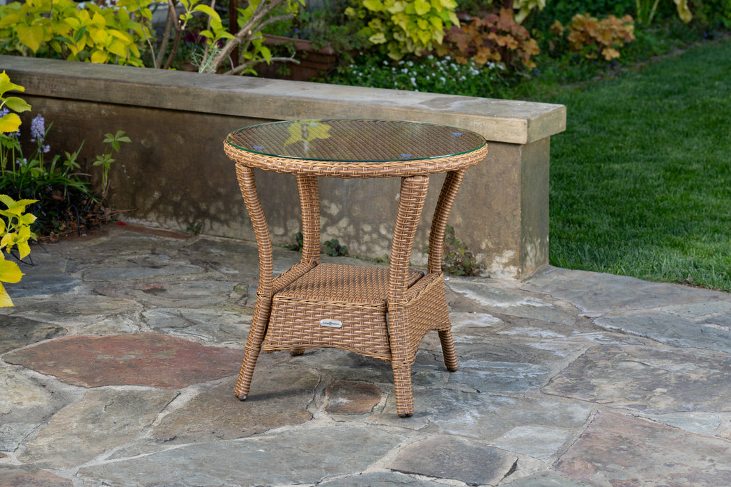 A luxury retreat patio with a Tortuga Outdoor Sea Pines 3-Piece Wicker Rocking Chair & Table Set, featuring a wicker side table on a stone patio.