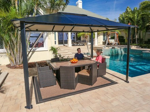 10x12 Durham Hard Top Gazebo beside a swimming pool, with a dining table set for two and a vibrant bowl of oranges centering the table.