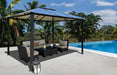 Paragon Outdoor Durham Hard Top Gazebo providing shade for a lounge area by a tropical poolside, with lush palms in the background.