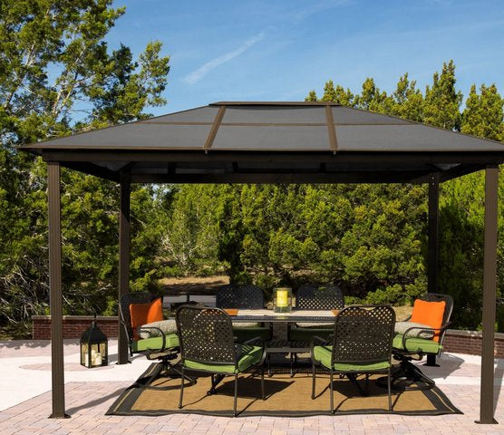 Paragon Outdoor Madrid Hard Top Gazebo on a patio with a full dining set and green and orange accents, set against a backdrop of lush greenery.