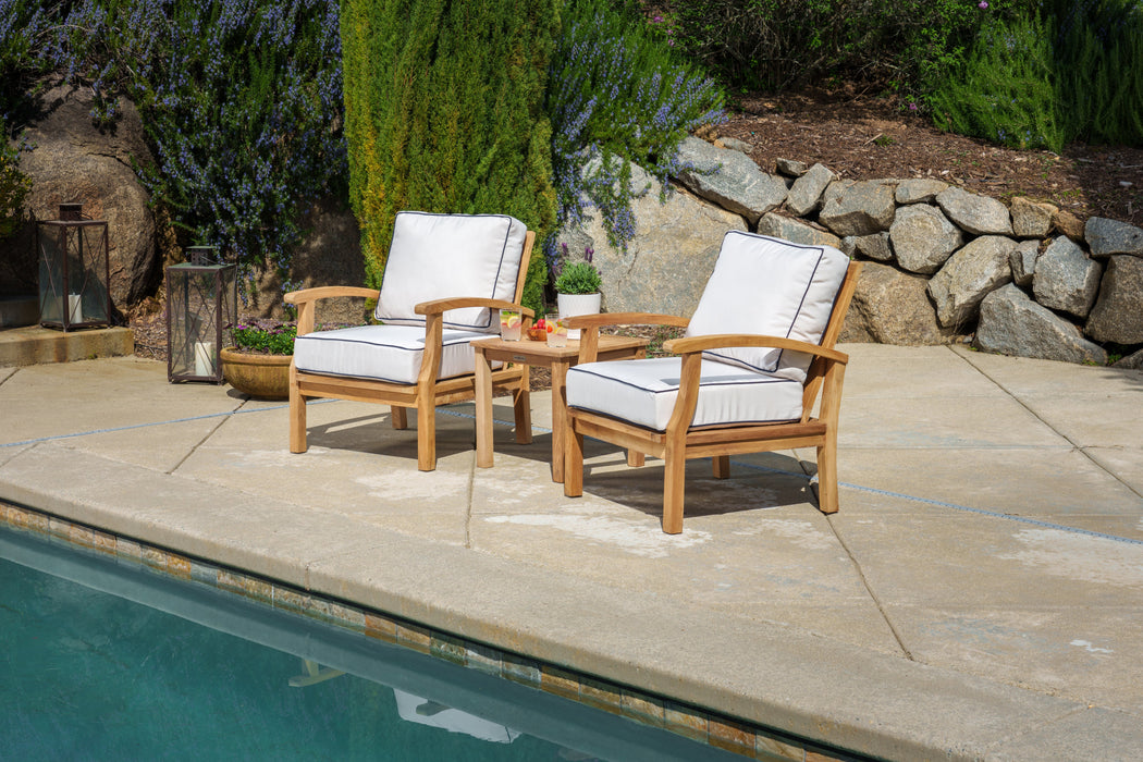 A luxurious retreat with a Tortuga Outdoor 3-Piece Indonesian Teak Club Chair Set, nestled beside a tranquil pool surrounded by a beautiful stone wall.