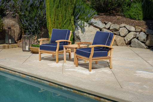 A Tortuga Outdoor 3-Piece Indonesian Teak Club Chair Set - Sunbrella Canvas Natural or Navy with a luxury retreat in the background.